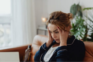 Woman sitting indoors with her hands on her temples, showing discomfort that may be associated with neck headaches.