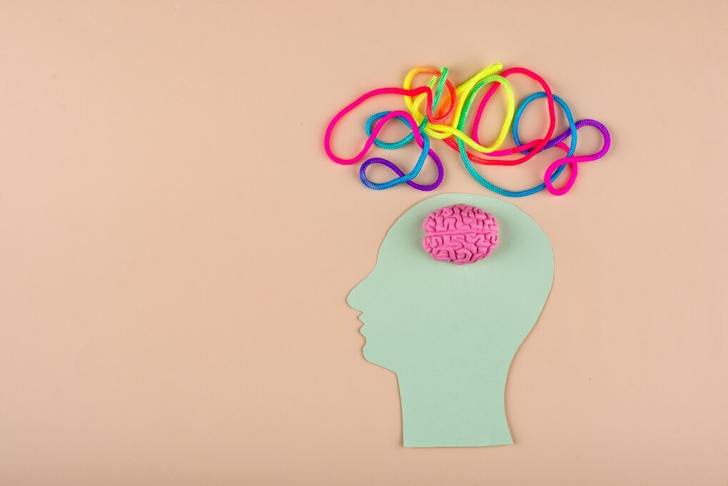 Paper head with a small brain and tangled colourful cords above it, symbolising disrupted brain and body communication in functional neurological disorder.