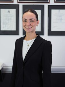 Professional portrait of Becca Villegas, Administrator at BHMC, wearing a black blazer and gold necklace, smiling confidently with framed qualifications visible in the background.
