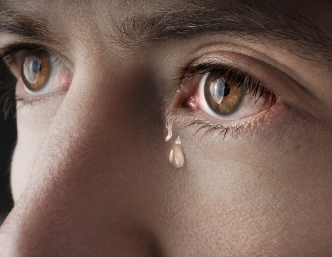 Close up of tear coming from man's brown eyes