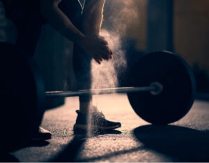 Close-up of an athlete preparing to lift a barbell in a dimly lit gym, symbolising intense physical exertion—a potential trigger for exertion headaches.