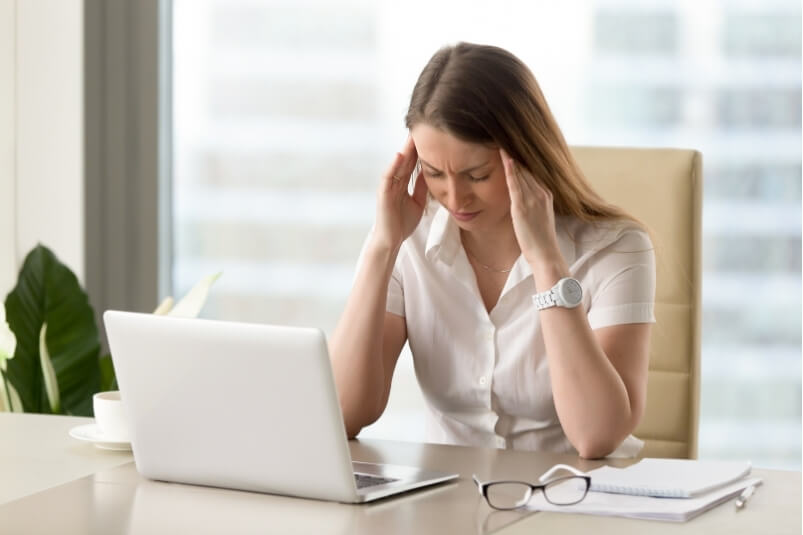 Woman experiencing a headache at her desk, highlighting need for headache relief physiotherapy