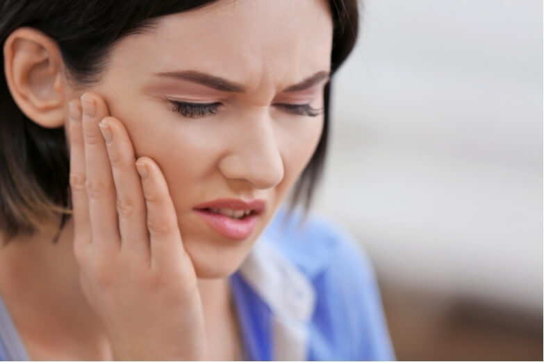 Close-up of a woman touching her jaw with a pained expression, highlighting discomfort from jaw clenching or temporomandibular joint (TMJ) issues.
