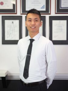Portrait photo of Marco Lin standing in front of a wall of certificates.