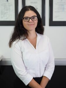 Portrait photo of Rebecca Lay standing in front of a wall of certificates.