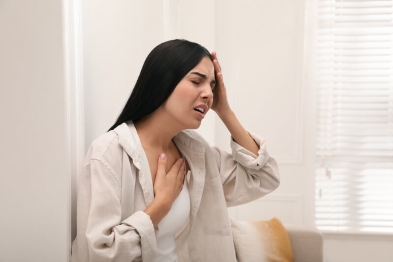 Woman experiencing headache and shortness of breath with migraine, holding head and chest in distress.